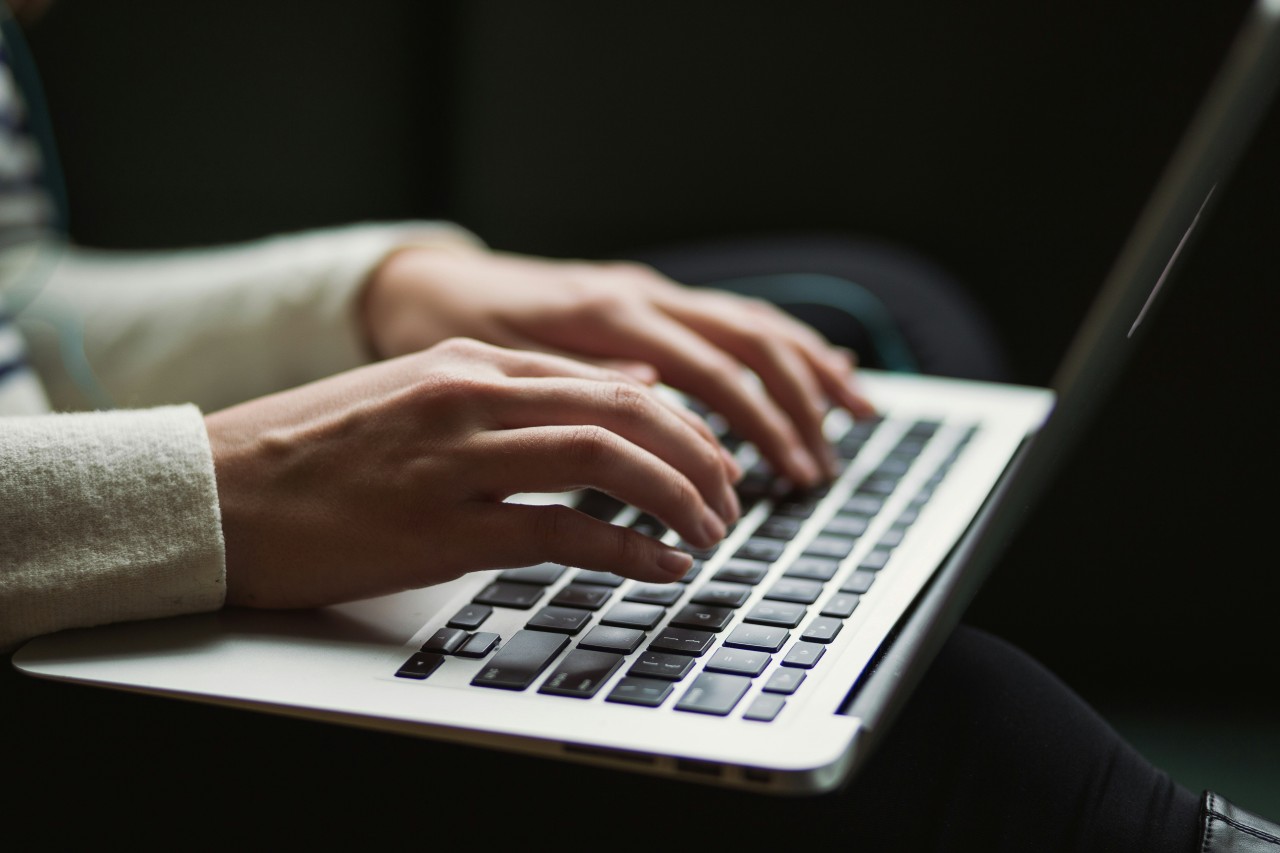 Close-up of hands typing on a laptop keyboard against a dark background.